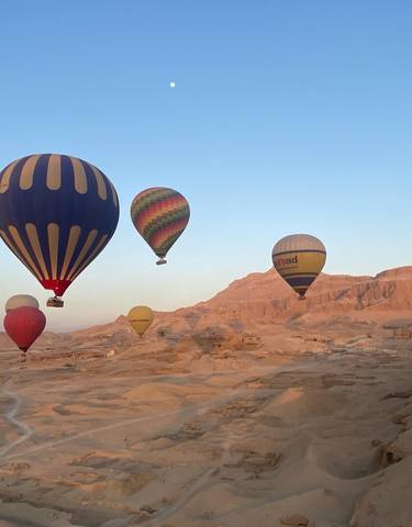 Hot air balloons floating over a desert landscape during sunrise.