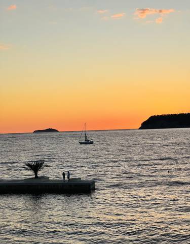 Sailboat on the sea at sunset with silhouetted cliffs.