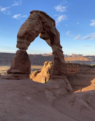 Person standing under a famous rock arch with rugged canyon views.