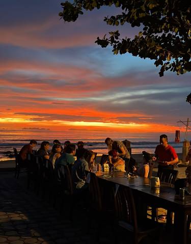 Group of people dining at a beachside restaurant during sunset.