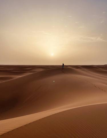 A lone person walking on sand dunes during sunset.