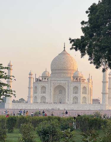 The Taj Mahal behind trees with people in the foreground.
