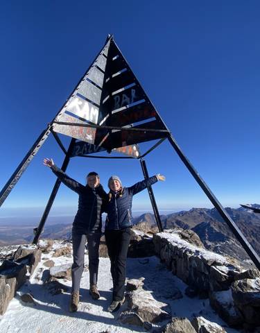 Two people at the peak of a mountain next to a metal structure.