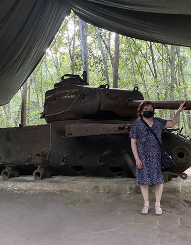 Person posing with a historic tank under a canopy.