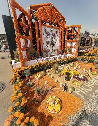Elaborate Day of the Dead altar with bright marigold flowers and fruit.