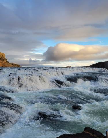 Wide waterfall with flowing water and cloudy sky.