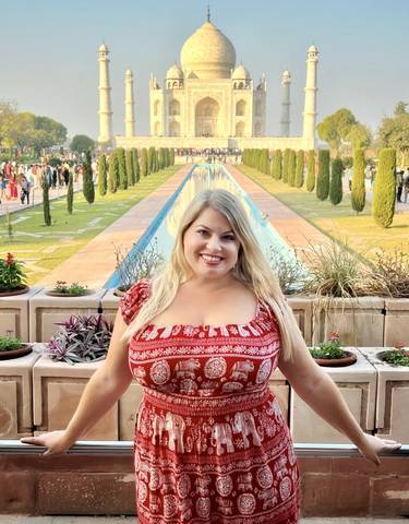 Smiling woman with long hair posing with a formal garden and pool in the background.