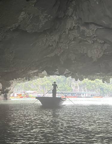 Person on a boat emerging from a cave with distant boats visible.
