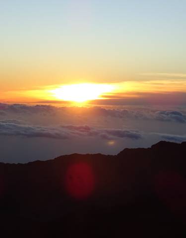 Sunrise view above the clouds with a silhouette of a mountain.