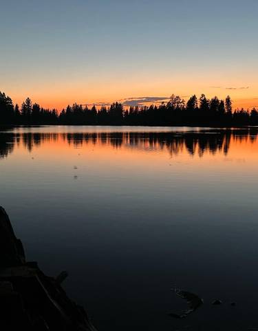 Sunset over a calm lake with reflective water and silhouettes of trees.