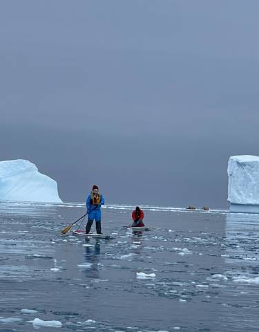 People stand-up paddleboarding among icebergs.