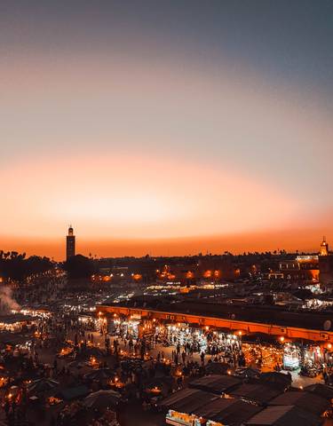 City skyline at sunset with minaret and buildings silhouetted against orange sky.