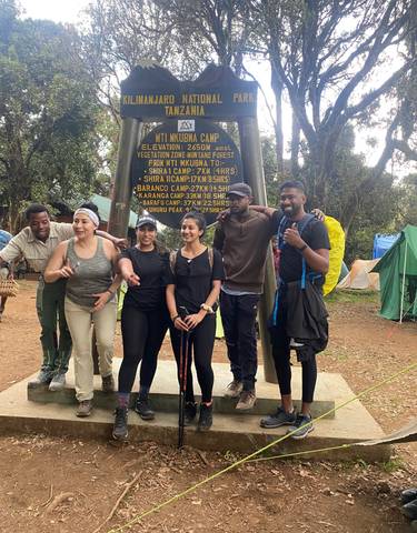 People posing with a sign indicating various camp distances.