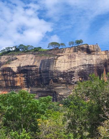 The Sigiriya Rock with trees below under a clear blue sky.