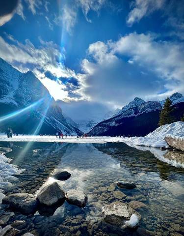 Sun shining over a frozen lake with a dramatic mountain view.