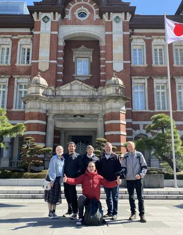 People posing in front of a historic building with Japanese flags.