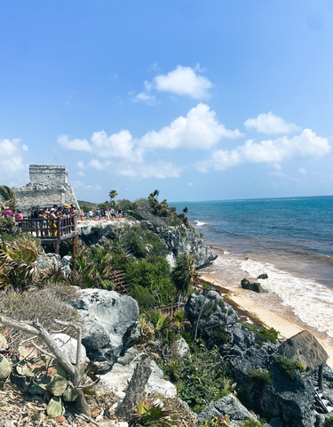 Tourists on a wooden deck overlooking the ocean at Tulum ruins.