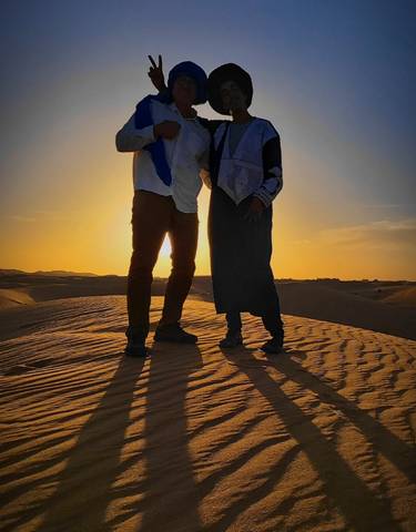 Couple walking on desert dunes during sunset.