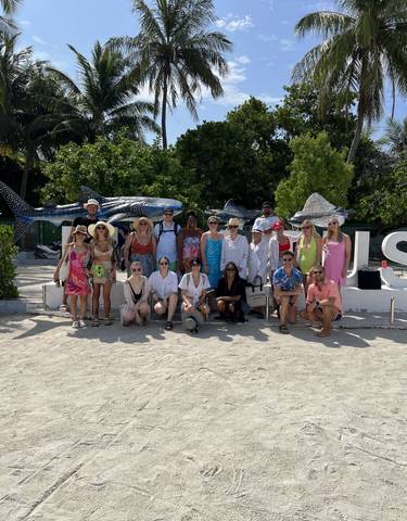 Large group of smiling people posing on the beach with marine life statues.