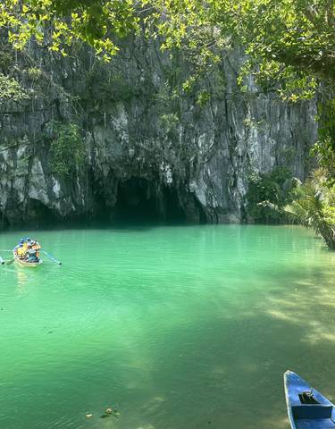 A small boat approaching a cave entrance surrounded by green water.