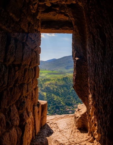 View through rock formations towards green hills and mountains.