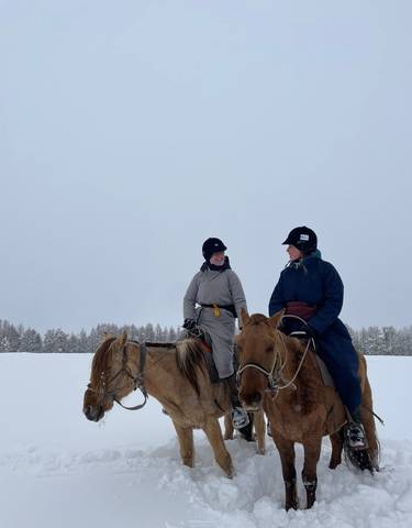 Two people on horseback in a snowy landscape.