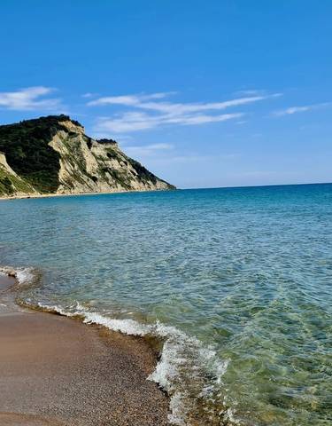 Pristine beach with cliffs and clear water under a blue sky.