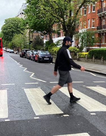 Person crossing a famous zebra crossing with red double-decker bus.