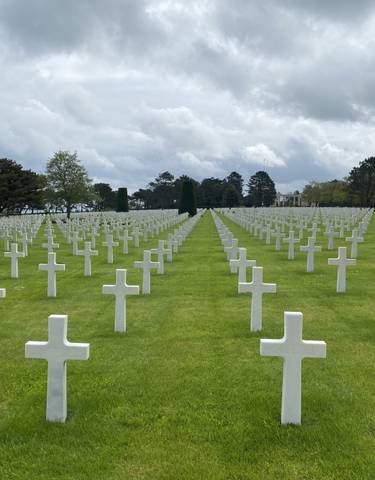 Cemetery with rows of white crosses and green lawn.