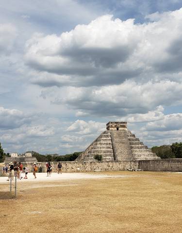 The pyramid of Chichen Itza with tourists under a cloudy sky.