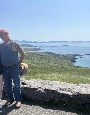 A couple standing in front of a scenic coastal landscape with islands visible in the distance.