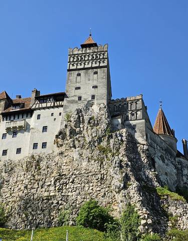 Bran Castle on a rocky cliff under a clear blue sky.
