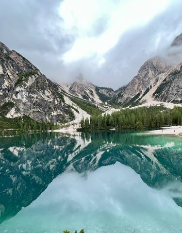 A stunning lake reflecting the surrounding mountains and trees under cloudy skies.