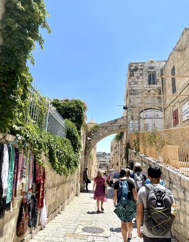 A bustling street with plants and a historic church archway.