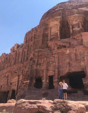 Ancient structure carved into red rock with two people posing.