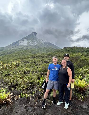 Three people posing in front of a volcano, lush landscape.