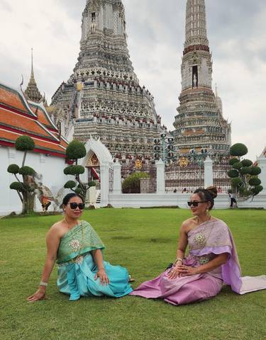 Two women in traditional attire in front of Wat Arun temple.