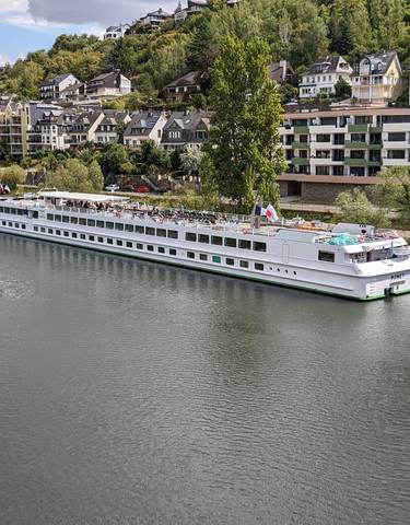 Large cruise ship docked on a river with colorful houses nearby.