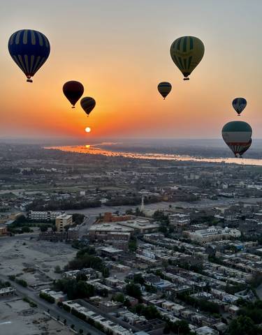 Hot air balloons floating over a city at sunset with a river in view.