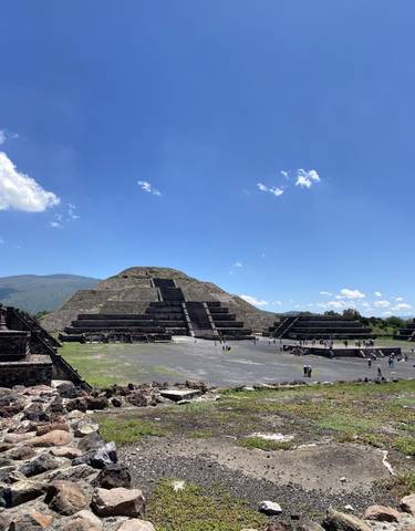 Stepped pyramid with people around, under a blue sky.