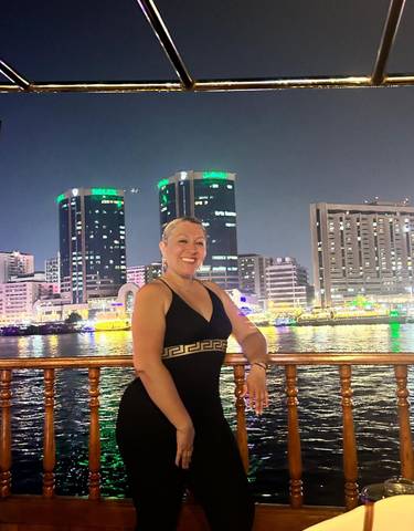 Person posing on a boat with a city skyline at night.