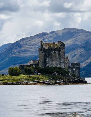 Historic stone castle by the water with mountains in the background.