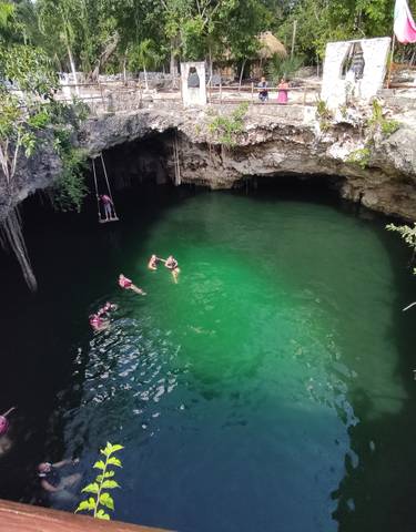 People swimming in a cenote with clear green water.