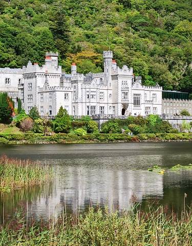 Kylemore Abbey reflecting in a calm lake surrounded by trees.