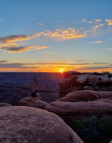 Person sitting on rocks enjoying the sunset view over a canyon.