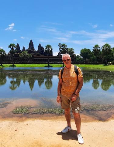 Person posing in front of Angkor Wat with reflective water in front.