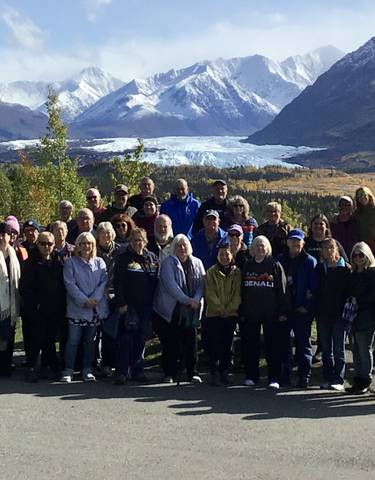A large group posing with a glacier and mountains in the background.