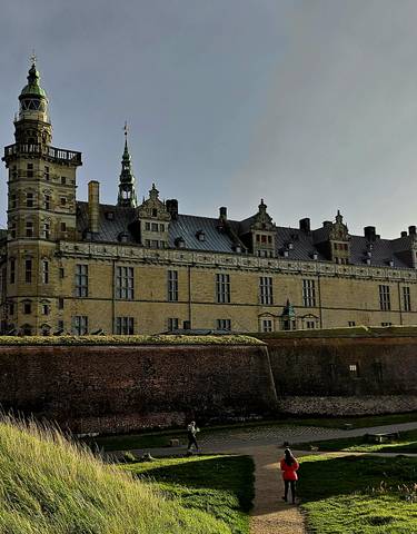 Historic castle viewed in a dramatic light with people walking below.