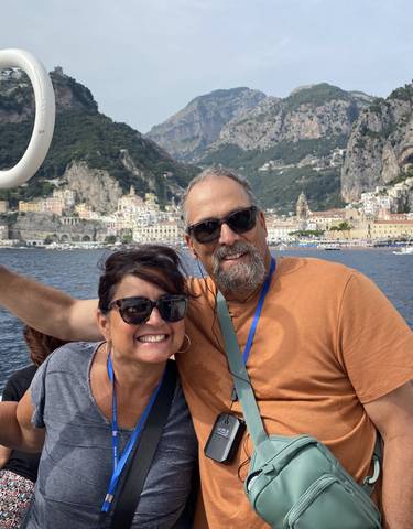 A couple smiling on a boat with the Amalfi Coast in the background.