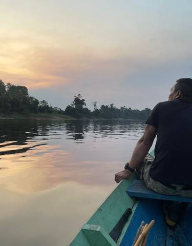 A person sitting on a boat looking at a sunset over a river with trees on the shore.